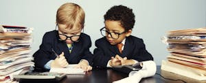 Two toddlers wearing suits and ties, surrounded by stacks of files, work with a calculator, pencil and notepad to determine if they have to pay the kiddie tax.