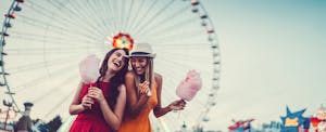 Two women eating cotton candy and laughing at the amusement park