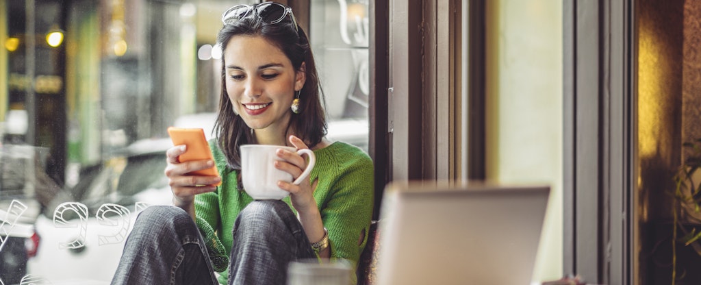 Young woman in a coffee shop drinking coffee and looking at her cell phone