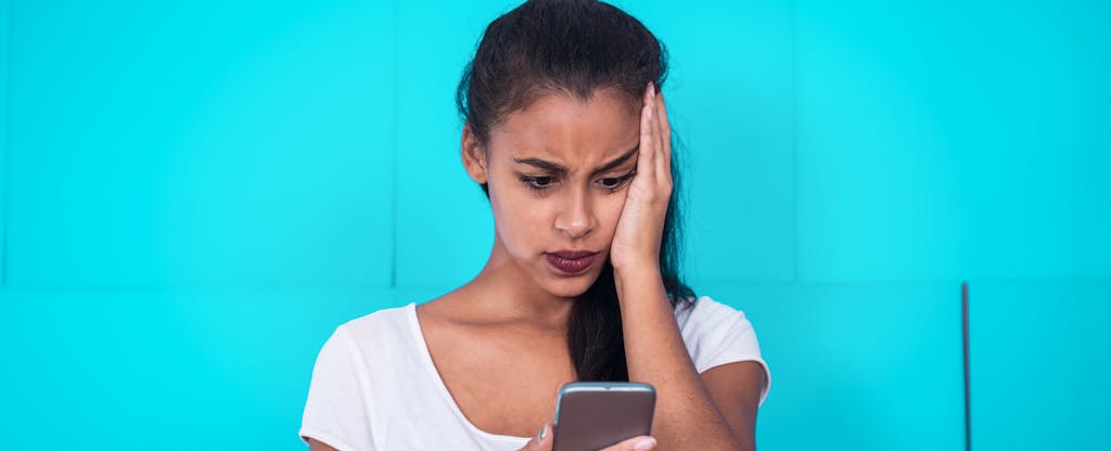 Young woman staring at phone and looking worried