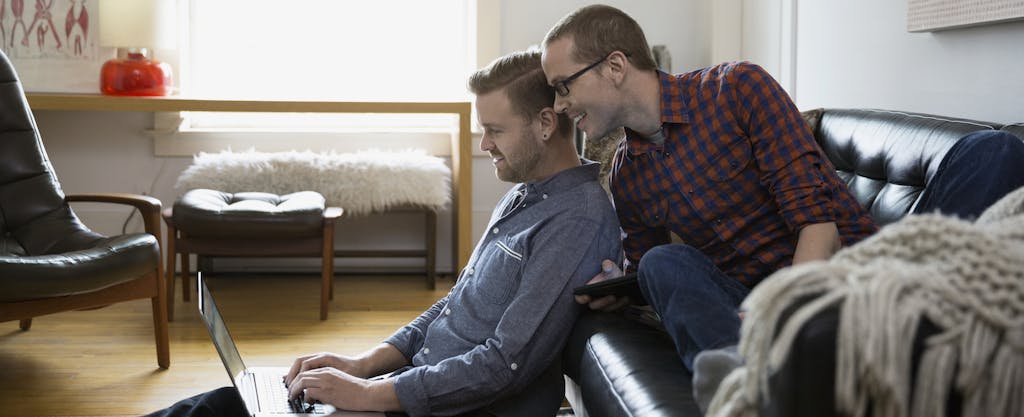 Young same-sex couple sitting in their living room doing their taxes on a laptop, ready to use the married filing jointly status for the first time.