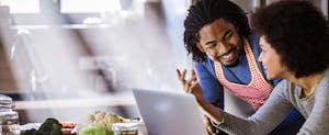 Happy African American couple talking while using laptop in the kitchen
