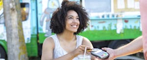 Smiling woman drinking cocktail and using credit card outdoors.