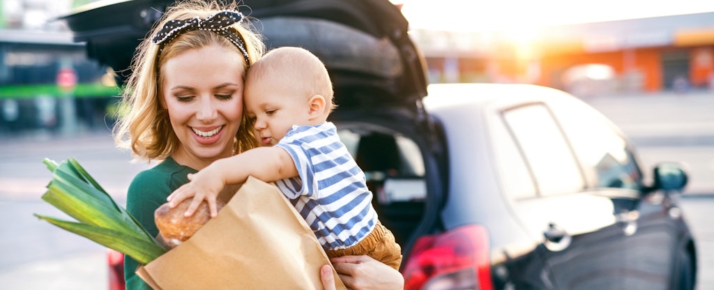 Woman holding her baby while loading groceries into her car