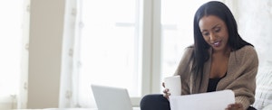 Woman sitting on her bed, drinking coffee and working
