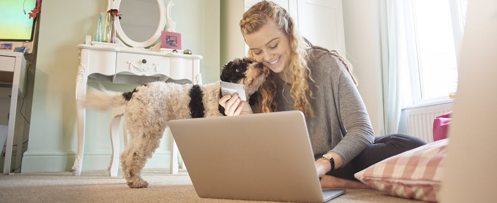 Young woman with her dog using her laptop on bedroom floor