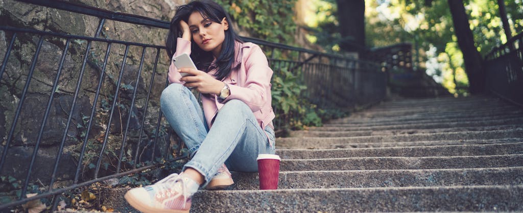 Unhappy young girl sitting on steps outside and texting