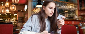 Young woman sitting in a cafe looking at her phone and making a payment with a credit card