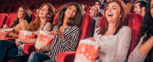 Happy young women eating popcorn and smiling in the cinema