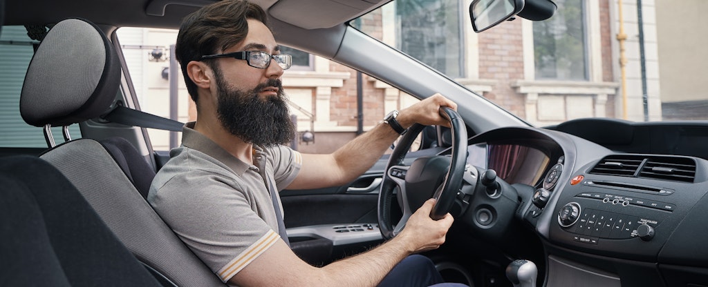 Young bearded man driving his car and smiling