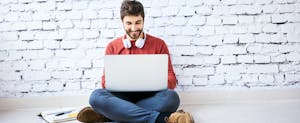 Male student sitting on floor with notebook and laptop studying