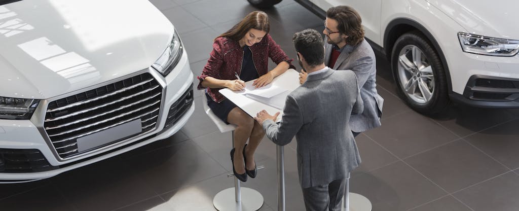 Couple signing the documents to buy a new car at a dealership