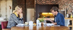 Couple working on their tax return on opposite sides of the kitchen table, trying to decide if they should use the married filing separately tax status.