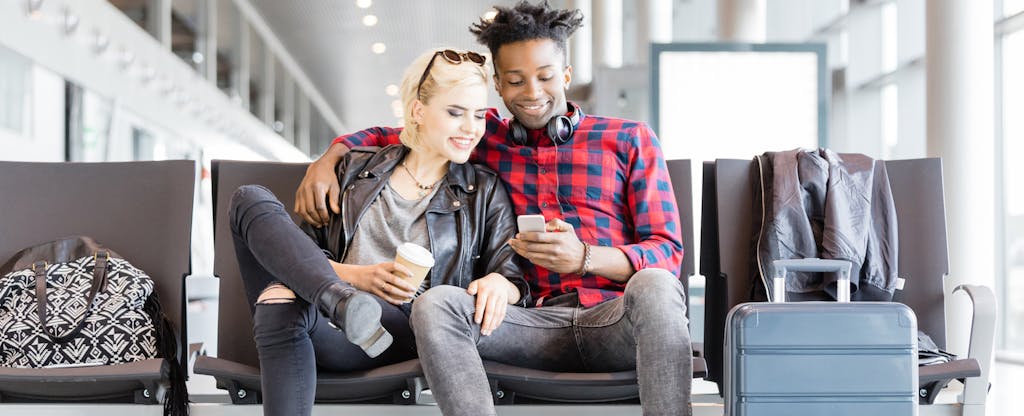 Young couple sitting on chair with suitcases in airport lounge