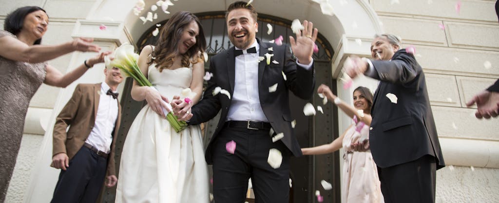 Friends throwing flower petals over bride and groom as they leave church.