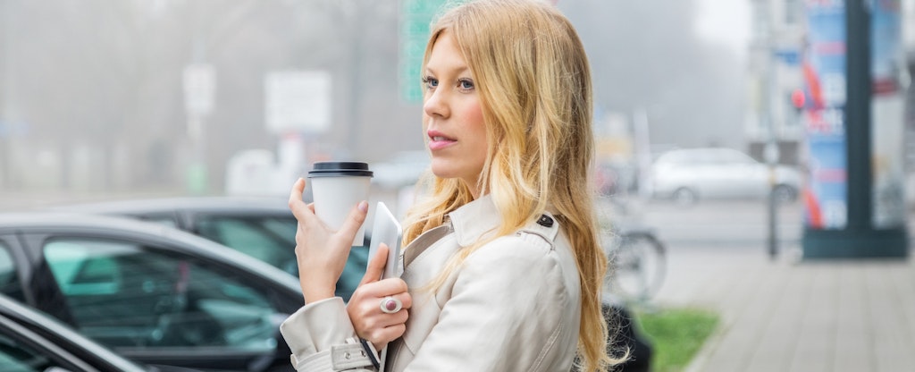 Young woman in city holding coffee and digital tablet