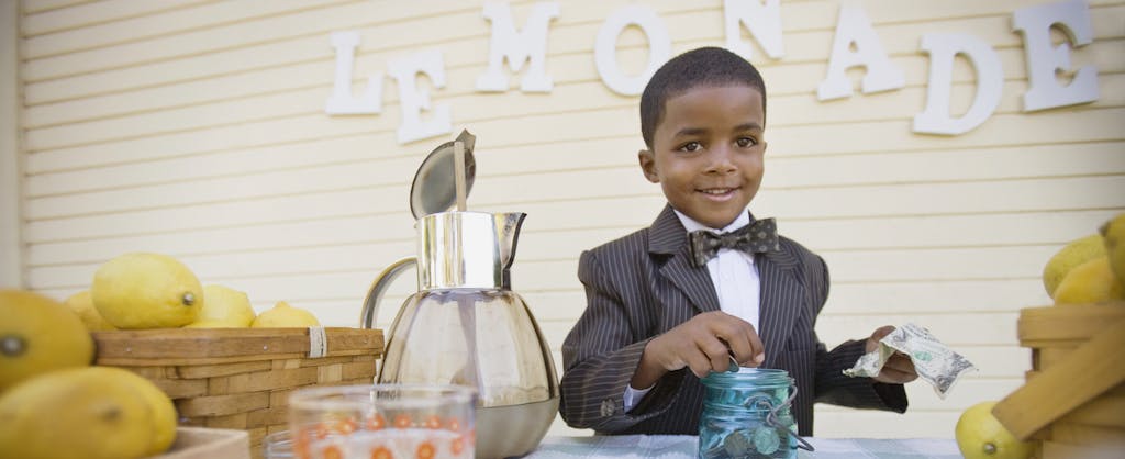 Young African-American boy, wearing a bowtie, and counting money from his lemonade stand, not worried about the possibility of having to file a dependent tax return.