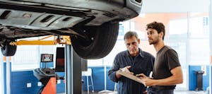 Middle-aged mechanic holding clipboard and discussing auto repair financing with young man