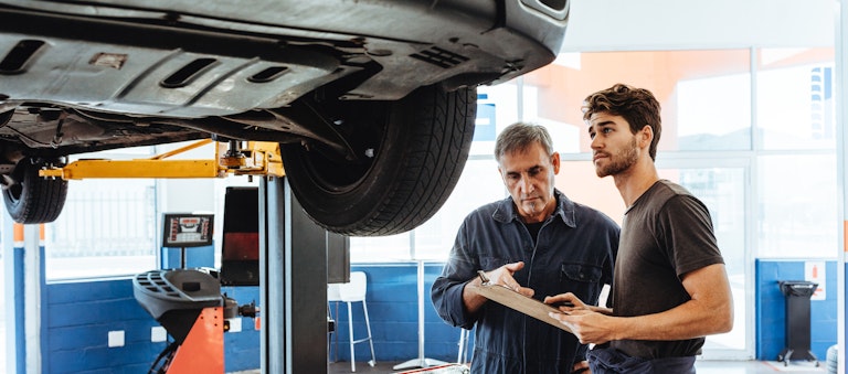 Middle-aged mechanic holding clipboard and discussing auto repair financing with young man
