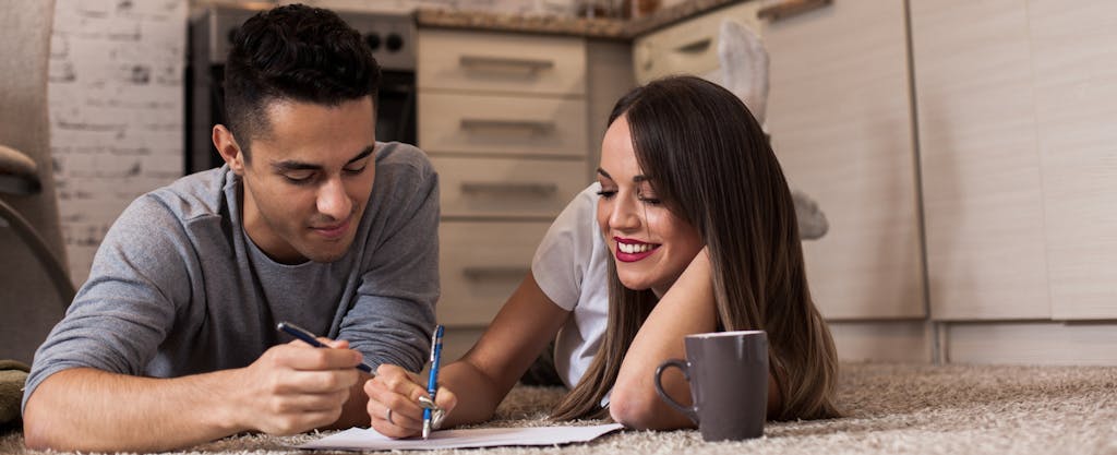 Young couple lying on the floor, drinking coffee and planning the best way to pay off their credit cards