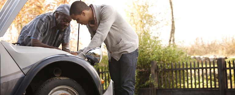 Two men outside looking at car motor