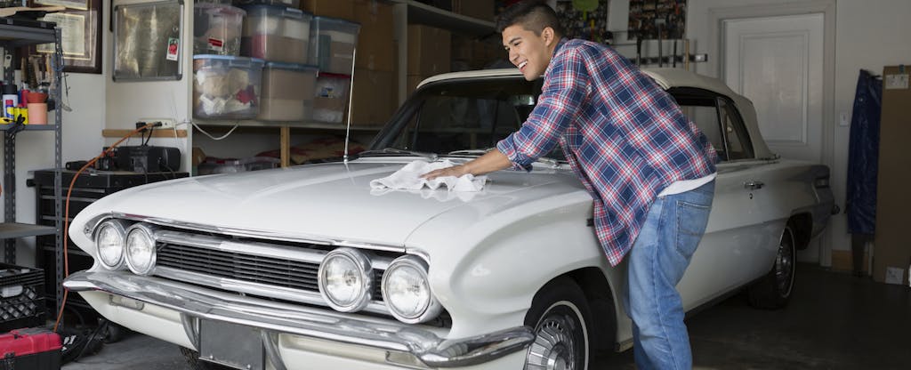 Young man waxing vintage car in garage
