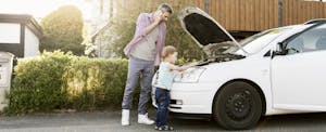 Man talking on the phone while standing outside of his broken-down car with his son