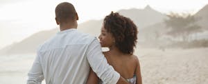 Woman looking over her shoulder as she walks on the beach, arm in arm with a man