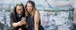 Two smiling Asian women posing for cell phone selfie