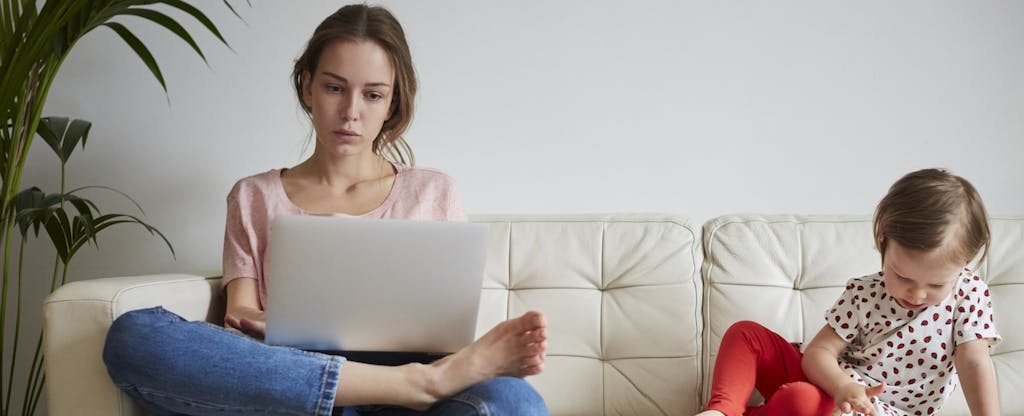 Woman sitting on the couch reading her laptop, with her child sitting next to her