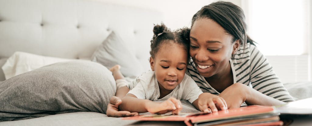 Mother reading to her toddler daughter in bed