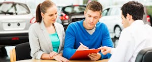 Couple filling out vehicle registration paperwork at car dealership