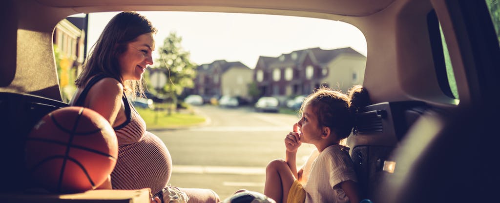 Woman sitting in the open trunk of her SUV, talking with her daughter