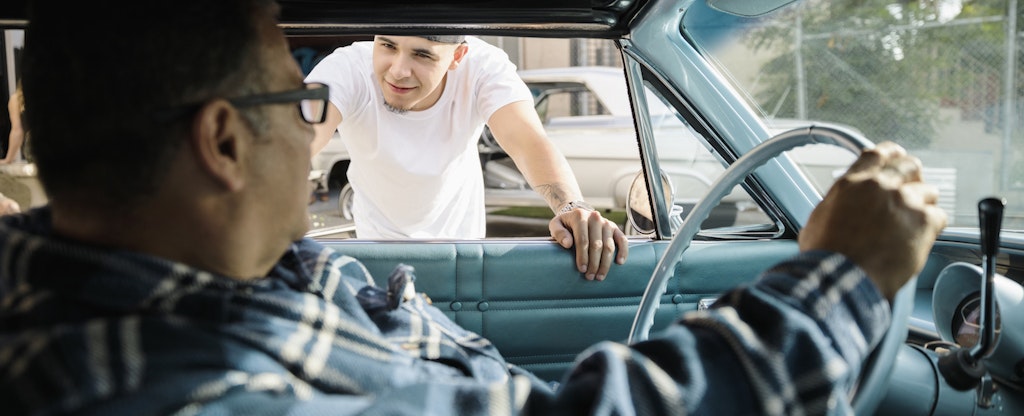 Man looking into the driver's side window of a car, talking to a man who is test driving the car