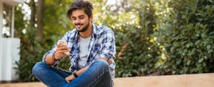 Young adult male sitting on the ground and texting on a mobile phone