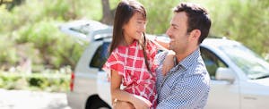 Father holding daughter outdoors with car in background