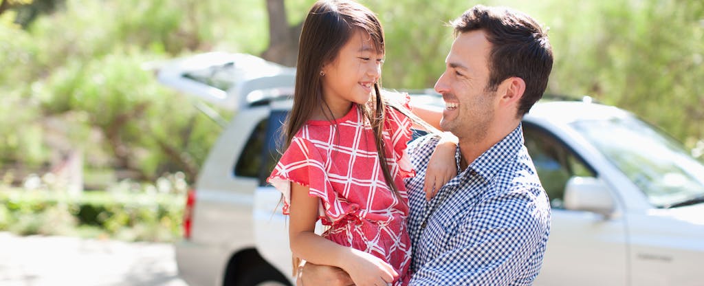 Father holding daughter outdoors with car in background