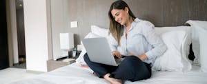 Businesswoman in hotel room sitting on bed and working on her laptop