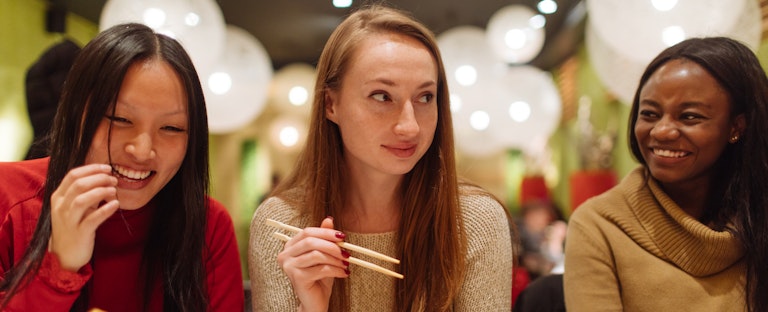 Group of female friends enjoying sushi together at a restaurant. One friend is going into debt to be able to go out with her friends.