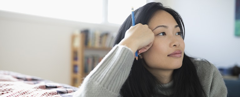 Woman leaning on her bed, resting her head on her hand and thinking