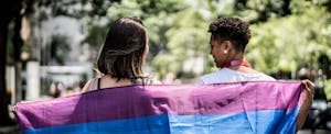 Two women walking together, with a Pride flag draped over their shoulders