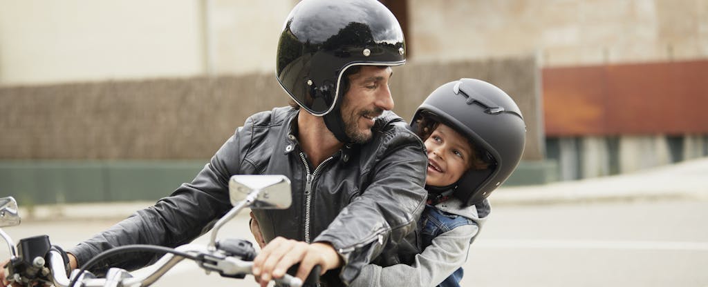 Man sitting on a motorcycle, with his child behind him