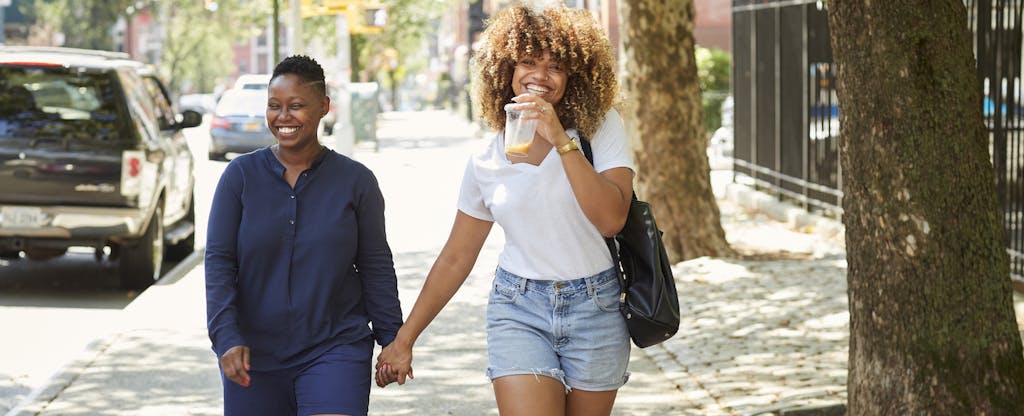 Two women walking together on a city sidewalk, smiling and holding hands