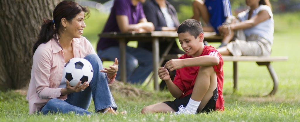 Mom sitting with young soccer player son outside at a park