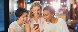 Three female friends out at night looking at cell phone
