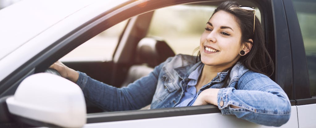 Smiling young woman driving car with window down