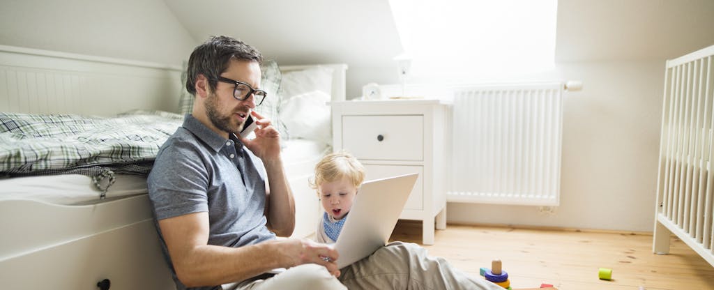 Man looking at his laptop while sitting on the floor with his toddler child