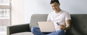 Young man sitting on couch and holding credit card to learn about a finance charge