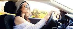 Young woman in hat and sunglasses driving her car