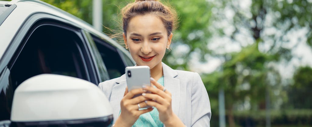 Young woman looking at cell phone to see how much her car is worth